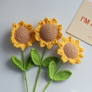 Three handmade knitted yellow sunflowers with green stems on a clean grey background