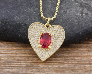 Macro shot of gold-plated heart pendant with red oval stone and sparkling zircons