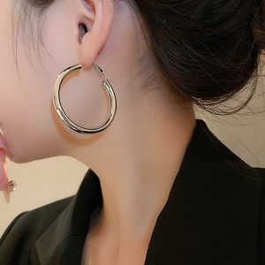 Macro shot of large polished silver hoop earrings on model with sleek metal texture
