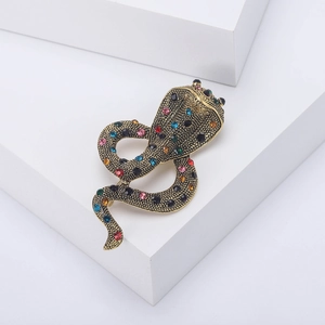 Vintage cobra brooch in gold alloy with colorful rhinestones on a white display block