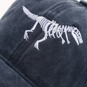 Navy blue cotton baseball cap featuring white dinosaur skeleton embroidery in a front view