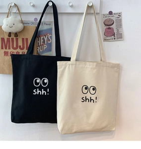 Detalle de bolsos tote de lona con divertidos ojos colgados en una pared blanca