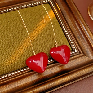 Detailed view of vintage gold earrings with glossy red heart pendants on a green fabric