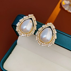Macro shot of hollow teardrop pearl earrings with zircon inlay on green velvet box