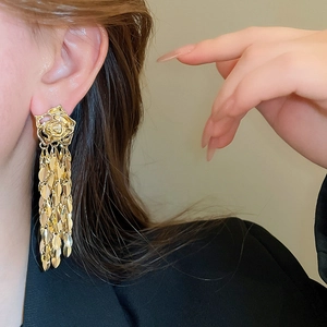 Detail of gold rose stud earring with long leaf tassel on model in black blazer