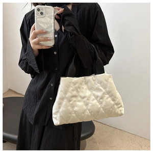 Close-up of a white quilted tote bag with black handles held by a model in a black shirt
