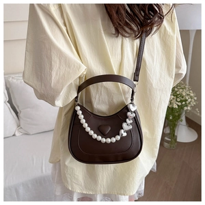 Brown crescent bag with pearl and silver heart chains shown on a model's shoulder