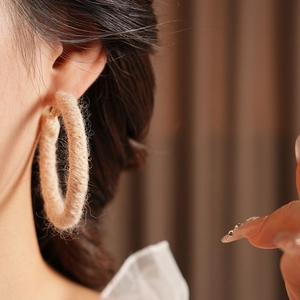 Dettaglio macro di un orecchino a cerchio in lana beige intrecciato a mano su una modella
