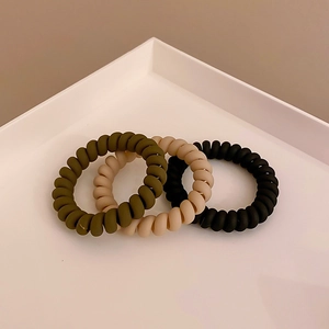 Three-pack of matte spiral hair ties in olive, beige, and black on a white tray