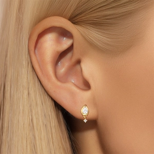 Close-up of golden bow stud earring with drop-shaped zircon and a small round diamond
