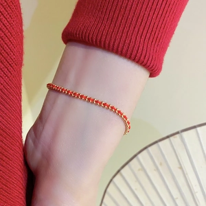 Detail of hand-woven red cord bracelet featuring gold-plated beads on a model wrist