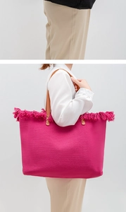 Fuchsia woven tote bag with brown leather handles and fringe detail shown on a model