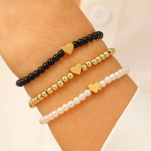 Primo piano di un set di braccialetti di perline con ciondoli a cuore dorati sul polso