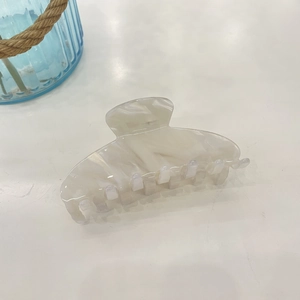Macro detail of pearl white acetate hair claw with elegant marble texture and smooth finish