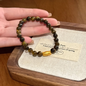 Detail of tiger eye bead bracelet with a gold animal head charm held by hand