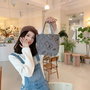Grey corduroy tote bag with black bear patterns and metal snap closure in a cafe setting