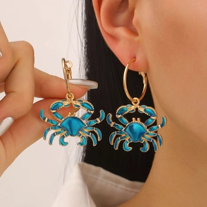 Detail of blue enamel crab dangle earring worn by a model with golden hoop base