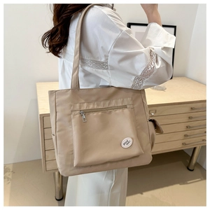 Detail of khaki tote bag showing the zipper pocket and round 'good luck' patch on canvas