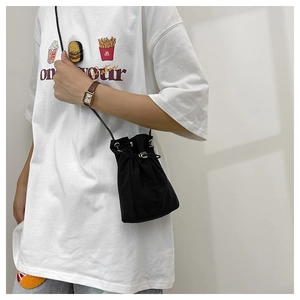 Detail showing a black nylon drawstring bucket bag worn cross-body for casual styling