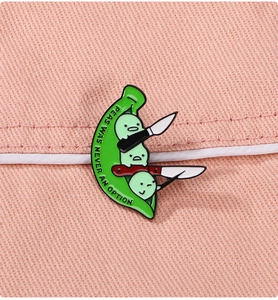 Détail du badge émaillé montrant des pois avec couteaux et texte humoristique anglais