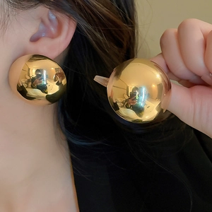 Close-up of model wearing large gold-finished polished metal sphere stud earrings