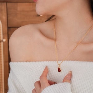 Close-up of a gold-plated necklace with a red double-sided gourd pendant on a model's neck