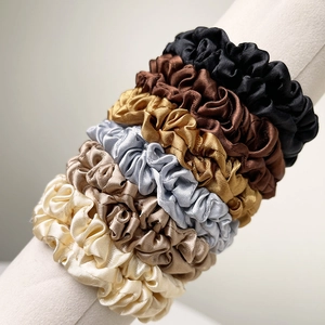 Close-up of six satin silk scrunchies in neutral earth tones on a display stand