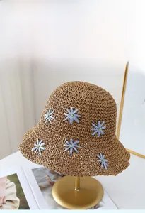 Detail of khaki straw hat featuring blue daisy embroidery on fine woven texture