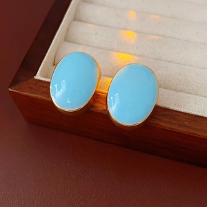Close-up of vintage oval turquoise stud earrings with gold plating on a velvet tray