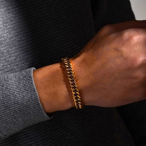 Close-up of a polished gold Cuban link bracelet worn on a male wrist with gray knit background