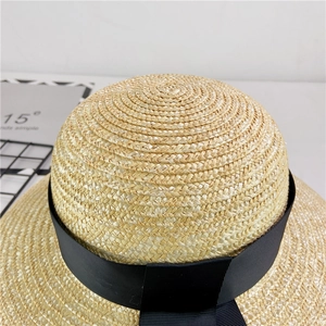 Top-down close-up of woven straw hat texture with elegant black ribbon and bow detail