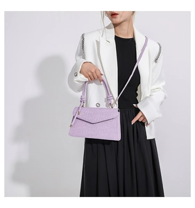 Detail of purple woven texture crossbody bag with gold hardware on a white blazer model