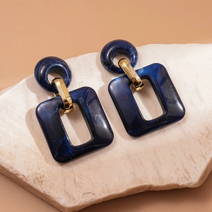 Detail of dark blue marble resin earrings on beige stone showing geometric square design