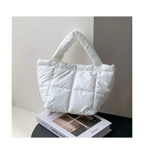 Detail of white quilted puffer handbag with padded texture on an artistic book background