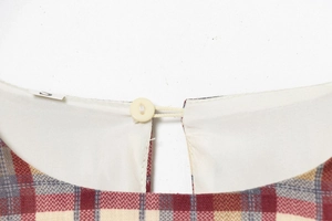 Dettaglio dello scollo dell'abito a quadri con trama in cotone e bottone bianco