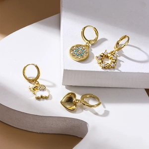 Artistic layout of gold huggie earrings with evil eye, elephant, and heart charms