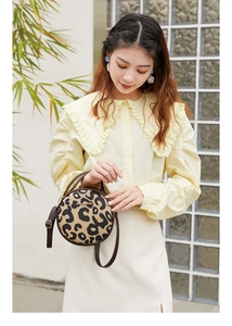 Detail of a round leopard print crossbody bag with leather trim and gold metal logo