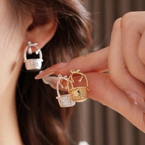 Detailed view of silver and gold bow basket earrings worn by model for size reference