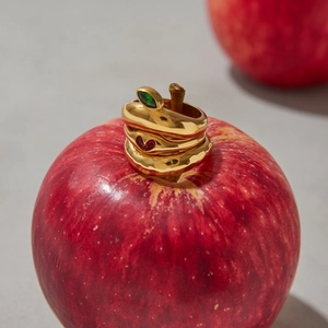 Detail of stacked gold rings with marquise green stone and red heart on an apple stem