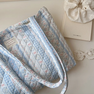 Detail of blue floral quilted tote bag featuring a pink bow and woven brand tag