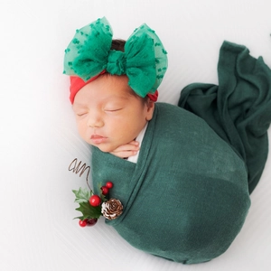 Detail of newborn wearing Christmas red nylon headband with green mesh bow and swaddle