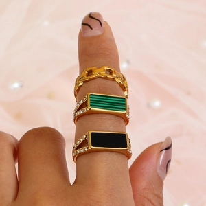 Close-up of golden stainless steel rings with green and black rectangular gems on hand