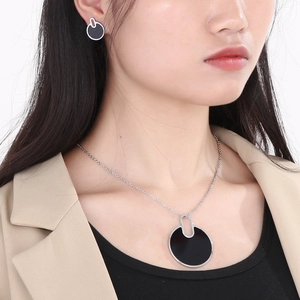 Close-up of black circular necklace and earrings set worn by a model in a beige blazer