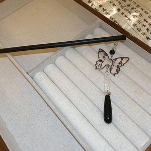 Detail of a butterfly tassel hair pin with black teardrop pendants on linen texture