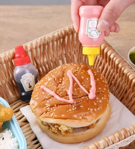 Mini plastic squeeze bottle dispensing pink salad dressing onto a fresh burger