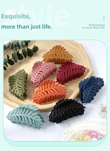 Macro shot of 8 leaf-shaped matte claw clips in assorted colors on a ceramic tray
