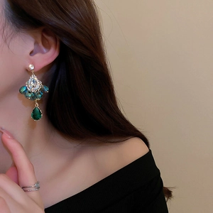 Close-up of elegant gold earrings with deep green teardrop crystals on model
