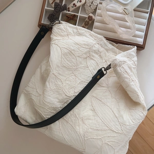 Detail shot of beige cotton tote bag with leaf embroidery and slim black leather strap