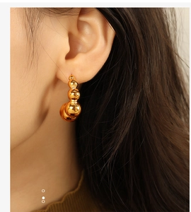 Detailed close-up of a model wearing golden pea-shaped beaded earrings with metallic luster