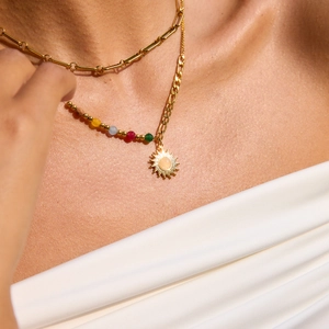 Close-up of stacked gold paperclip chain and sun pendant necklace with colorful beads